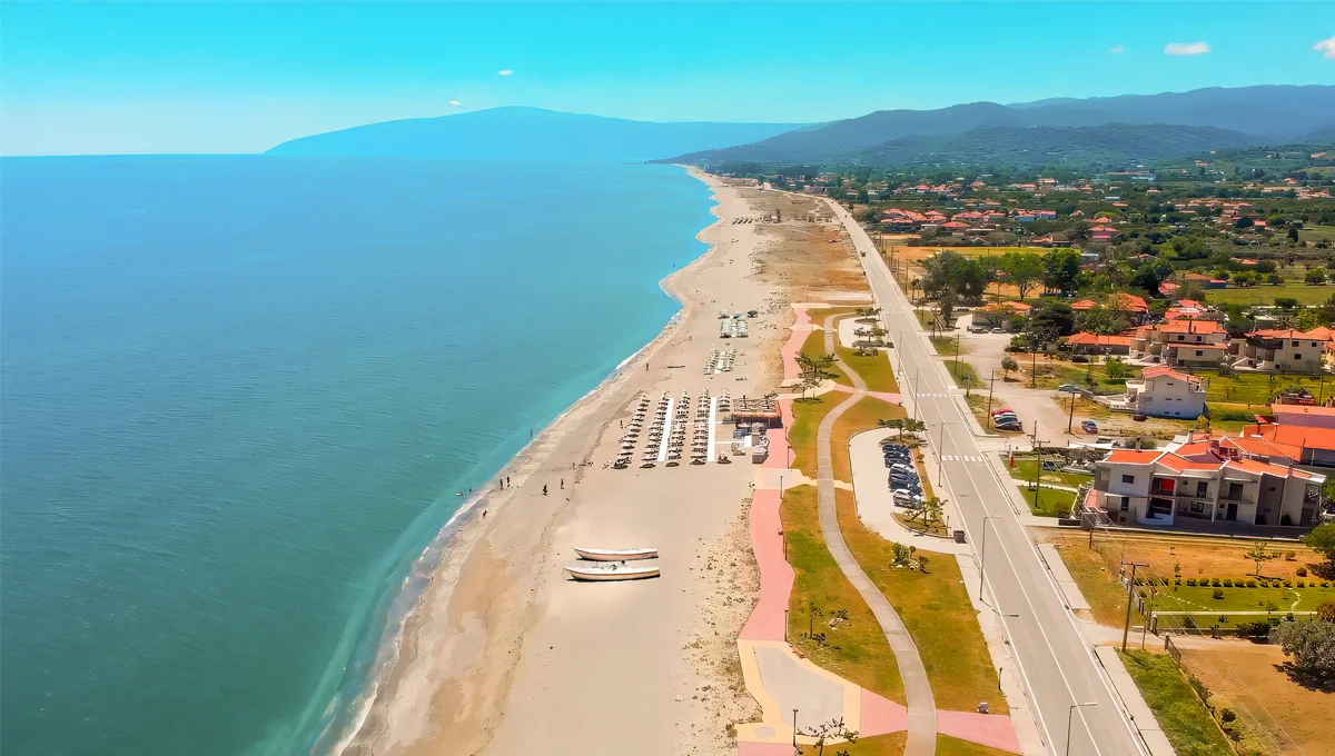 Εναέρια άποψη της μεγάλης, οργανωμένης παραλίας Κάτω Σωτηρίτσας, με άμμο, ξαπλώστρες και παραθαλάσσιο δρόμο με οικήματα.