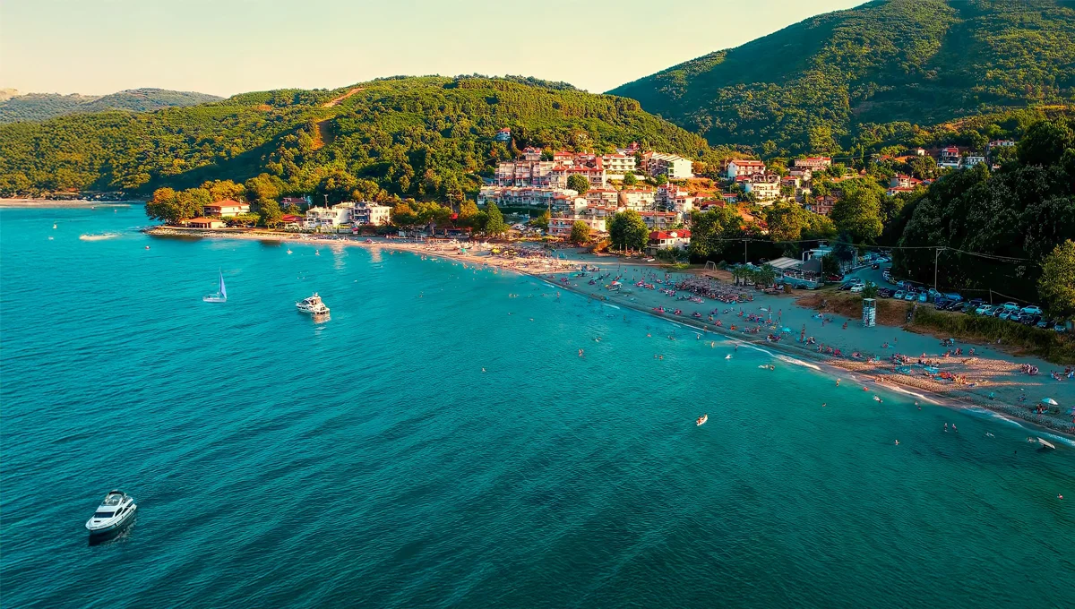 Πανοραμική θέα της παραλίας Κουτσουπιάς στην Αγιά, με σπίτια, βλάστηση και σκάφη στα γαλαζοπράσινα νερά.