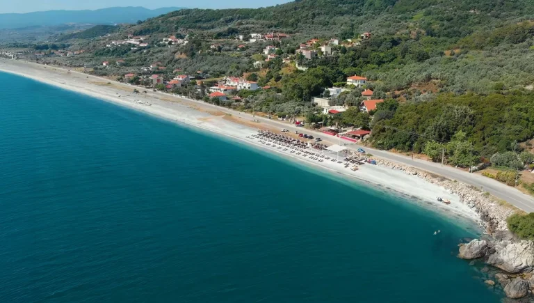 Εναέρια πανοραμική άποψη της μεγάλης, πετρώδους παραλίας Βελίκας στη Λάρισα, με γαλαζοπράσινα νερά και παραθαλάσσια σπίτια.