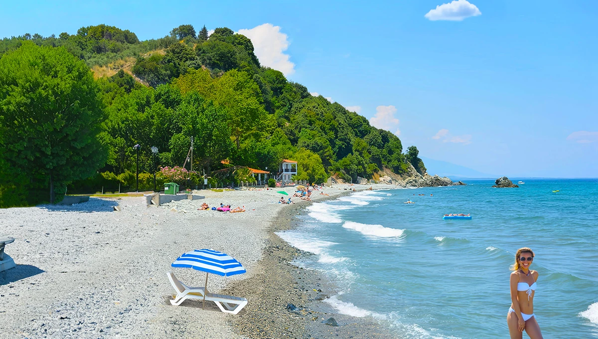 Πλατιά άποψη της Παραλίας Κόκκινο Νερό, με βότσαλα, θάλασσα και καταπράσινη βλάστηση. (Wide view of Kokkino Nero Beach, with pebbles, sea, and lush greenery.)