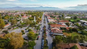 Αεροφωτογραφία του Αμπελώνα Λάρισας με την κεντρική λεωφόρο, πάρκο, εκκλησία και κατοικίες, με φόντο βουνά.