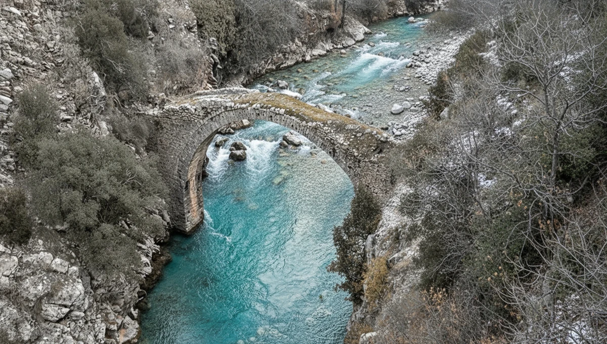 Παλιό μονότοξο πέτρινο γεφύρι Αργιθέας με γαλαζοπράσινα νερά ποταμού και βραχώδη όχθη.