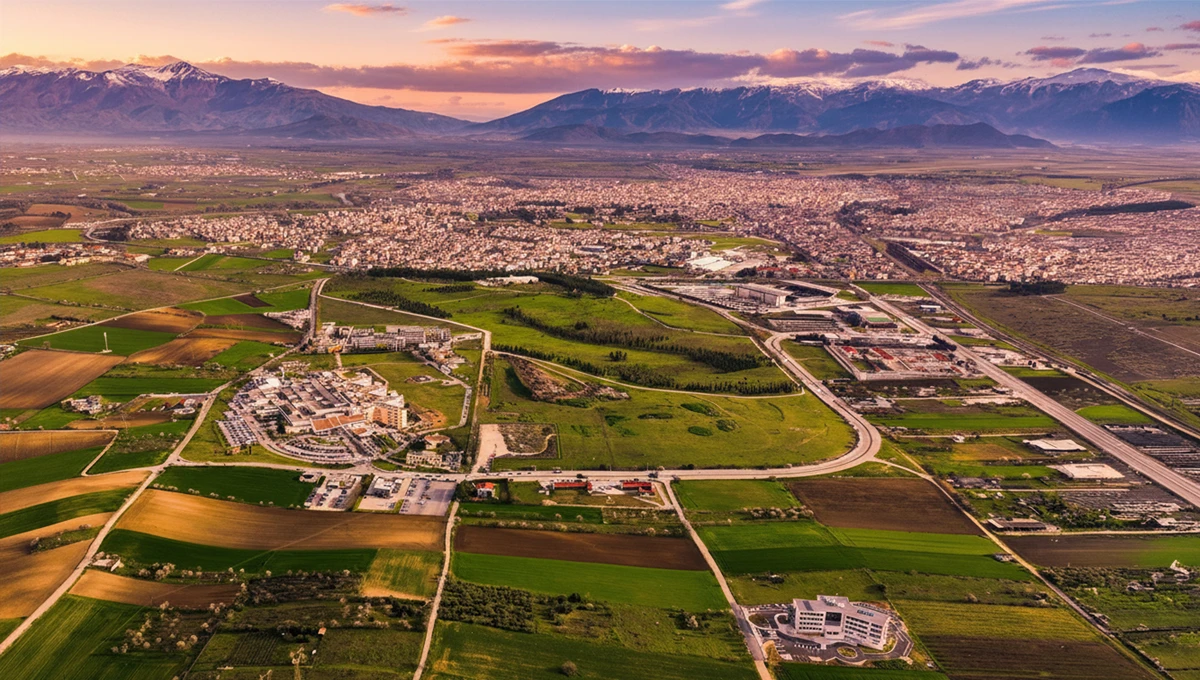 Πανοραμική αεροφωτογραφία της πόλης της Λάρισας να απλώνεται στον Θεσσαλικό κάμπο, με καλλιεργήσιμες εκτάσεις και χιονισμένα βουνά στο βάθος.