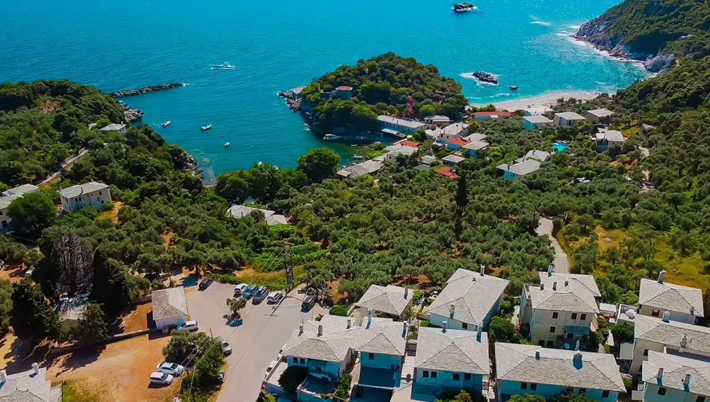 Πανοραμική εναέρια λήψη του φυσικού όρμου της Νταμούχαρης στο Πήλιο, με παραδοσιακά σπίτια και αγκυροβολημένες βάρκες στα καταπράσινα νερά.