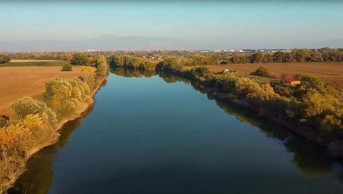 Ο Ποταμός Πηνειός στη Λάρισα, με ήρεμα νερά και πυκνή φθινοπωρινή βλάστηση στις όχθες του, κάτω από γαλάζιο ουρανό.