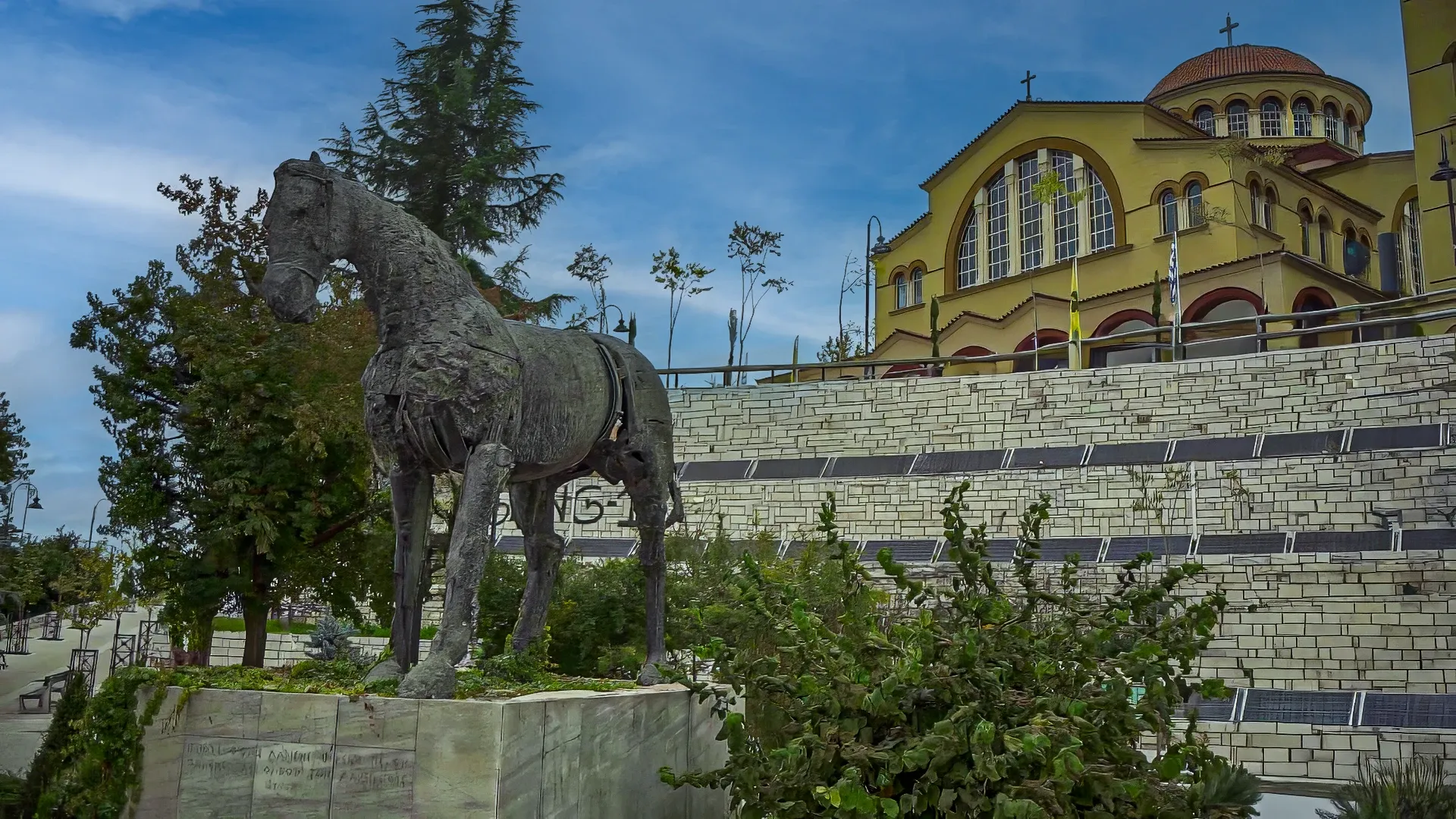Άγαλμα αλόγου, σύμβολο της Λάρισας, με φόντο τον Μητροπολιτικό Ιερό Ναό του Αγίου Αχιλλίου.