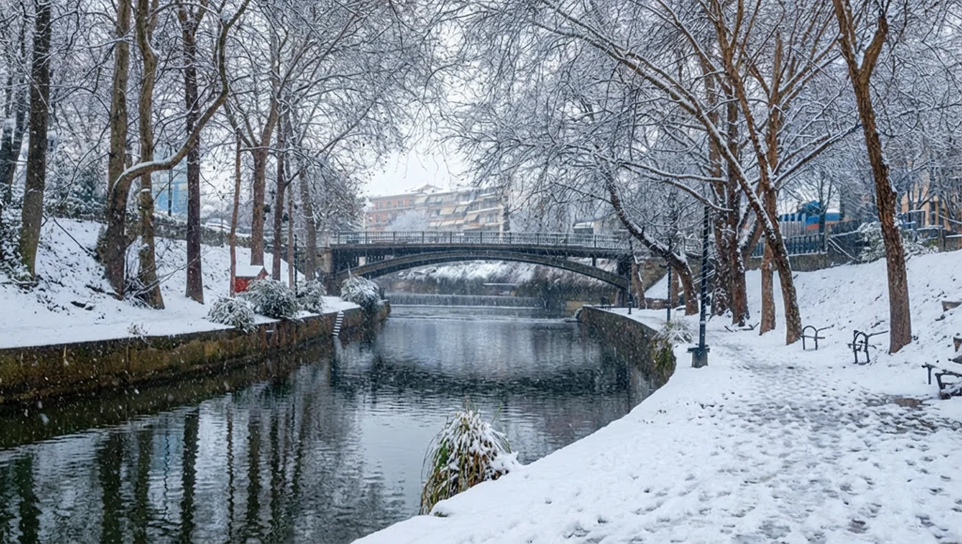 Η κεντρική μεταλλική γέφυρα στον Ληθαίο ποταμό στα Τρίκαλα με χιονισμένες όχθες και αντανακλάσεις στο νερό.