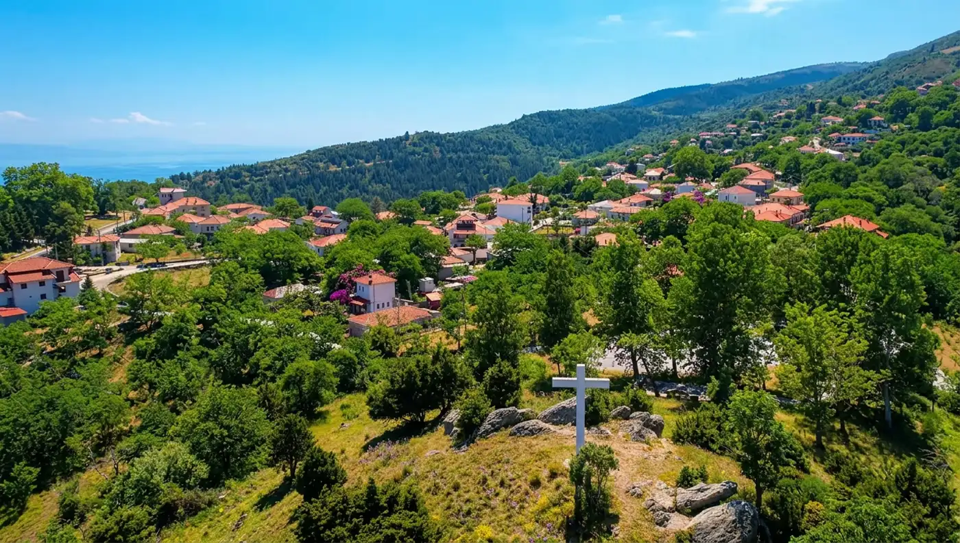 Πανοραμική λήψη του χωριού Ανατολή Αγιάς στην Όσσα με έναν μεγάλο λευκό σταυρό σε πρώτο πλάνο στην κορυφή του λόφου.