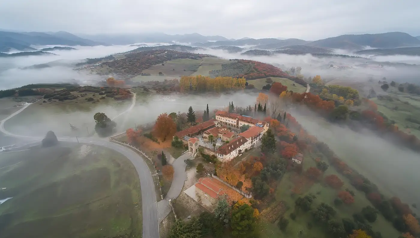 Πανοραμική αεροφωτογραφία με drone της ιστορικής Ιεράς Μονής Αναλήψεως του Σωτήρος στη Συκέα Ελασσόνας, περιτριγυρισμένη από φθινοπωρινή ομίχλη και φυσικό τοπίο.