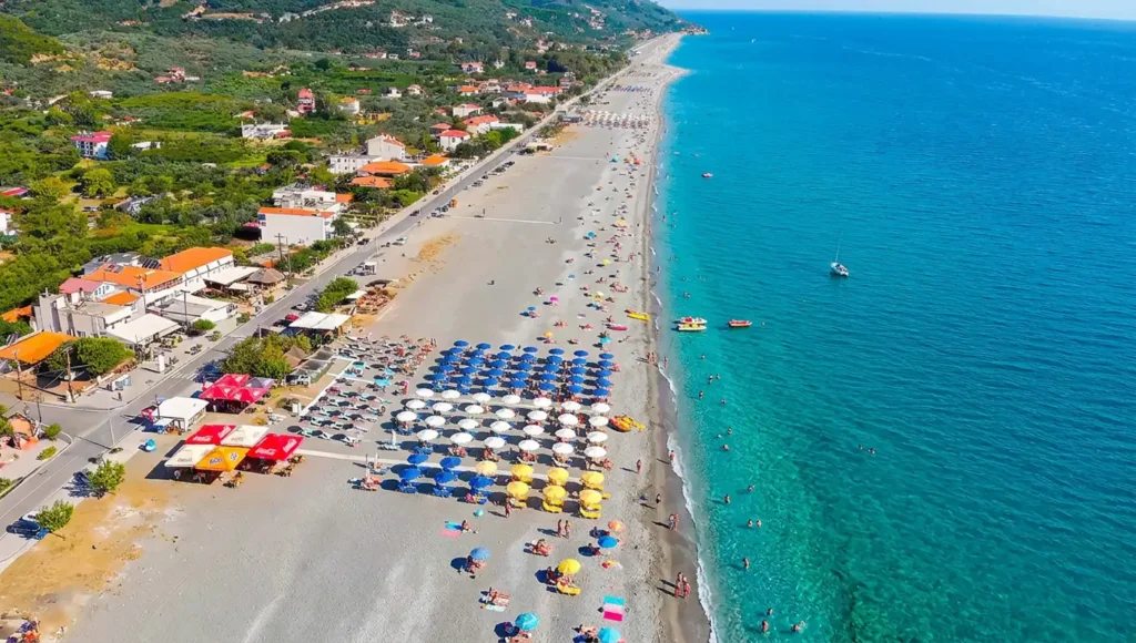 Πανοραμική εναέρια λήψη της τεράστιας οργανωμένης παραλίας στη Βελίκα Λάρισας, με ομπρέλες, καταγάλανα νερά και τον παραλιακό δρόμο.