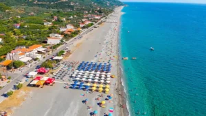 Πανοραμική εναέρια λήψη της τεράστιας οργανωμένης παραλίας στη Βελίκα Λάρισας, με ομπρέλες, καταγάλανα νερά και τον παραλιακό δρόμο.