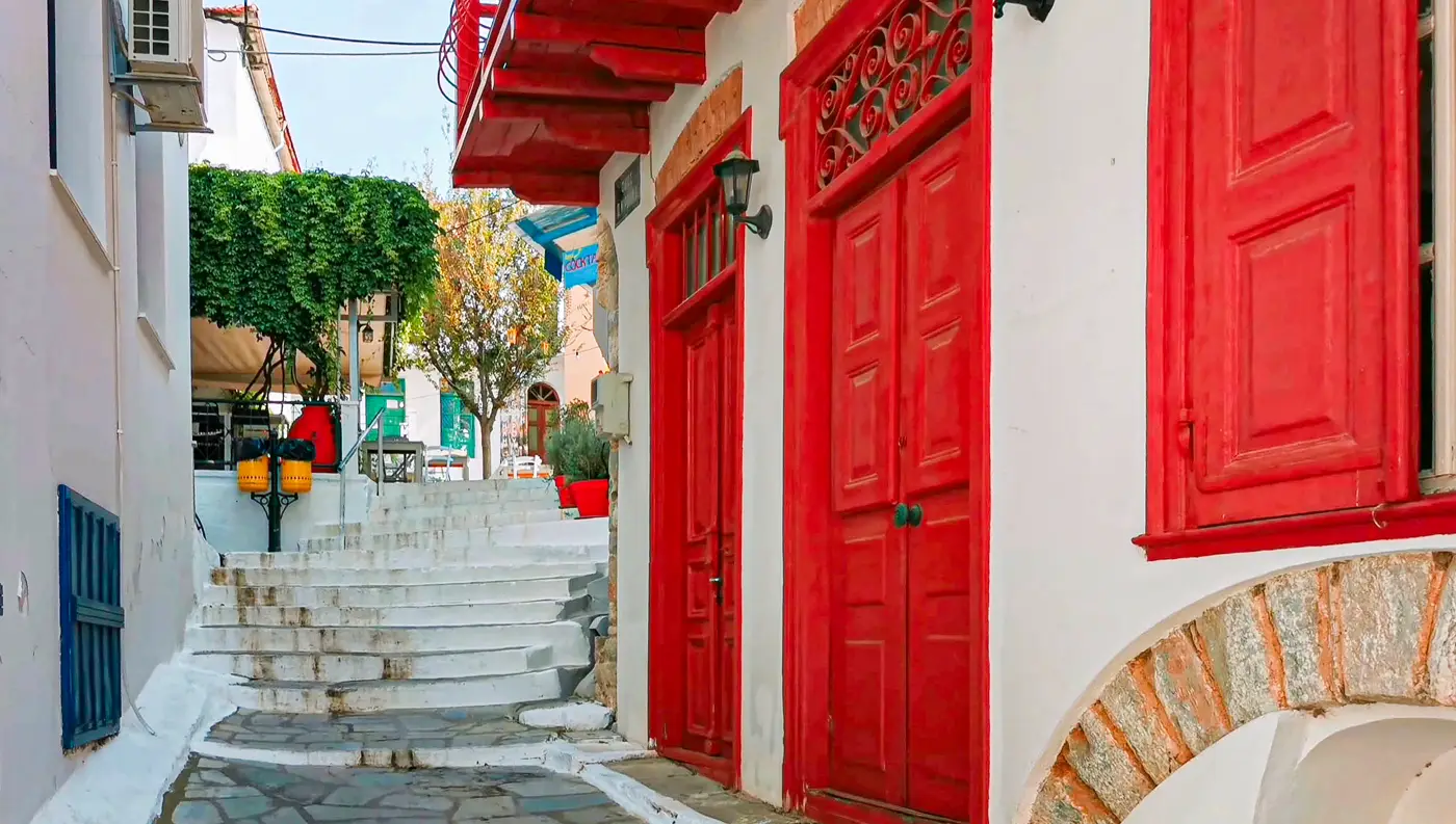 Πλακόστρωτο στενό καλντερίμι με παραδοσιακά λευκά σπίτια και πολύχρωμα παραθυρόφυλλα στο χωριό Γλώσσα της Σκοπέλου.