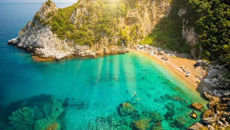 Θέα της παραλίας Φακίστρα με τα σμαραγδένια νερά μέσα από τα δέντρα, κατά τη διάρκεια της κατάβασης από το γραφικό μονοπάτι.