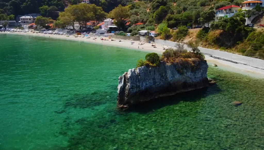 Πανοραμική drone λήψη του οικισμού και της παραλίας Καμάρι στο βόρειο Πήλιο, περικυκλωμένη από πυκνά δέντρα και γαλαζοπράσινα νερά.