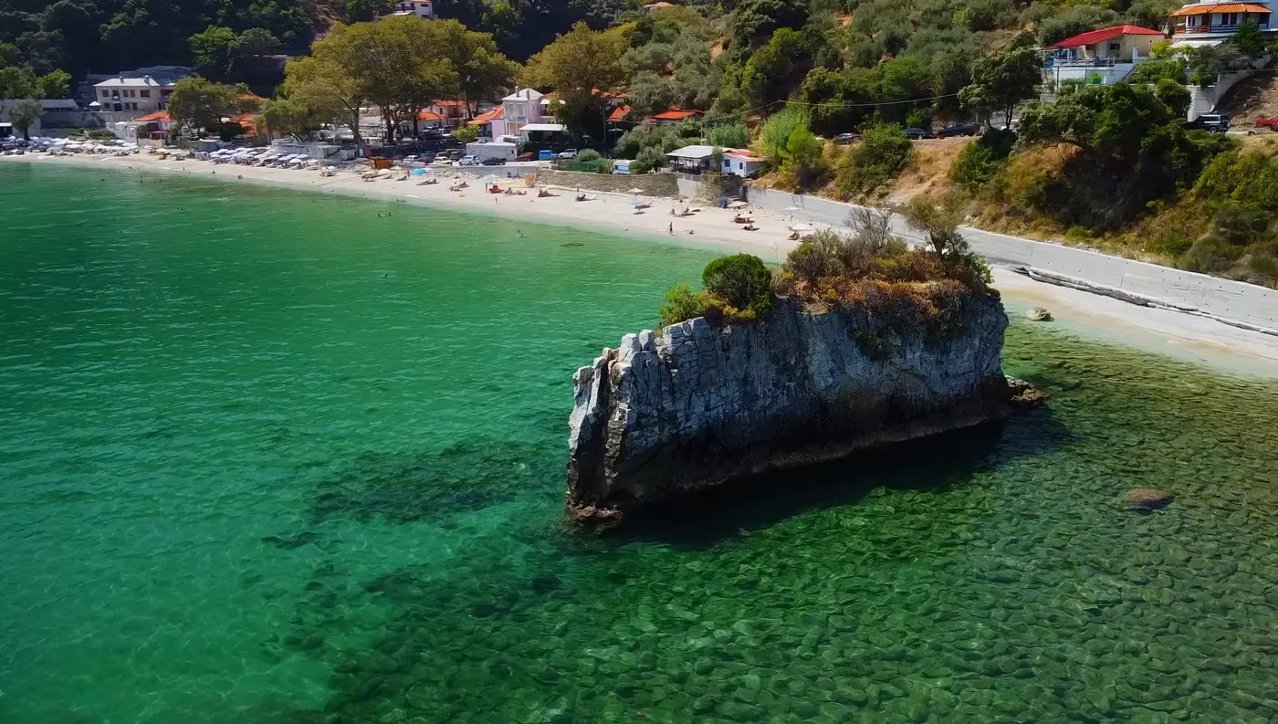 Πανοραμική drone λήψη του οικισμού και της παραλίας Καμάρι στο βόρειο Πήλιο, περικυκλωμένη από πυκνά δέντρα και γαλαζοπράσινα νερά.