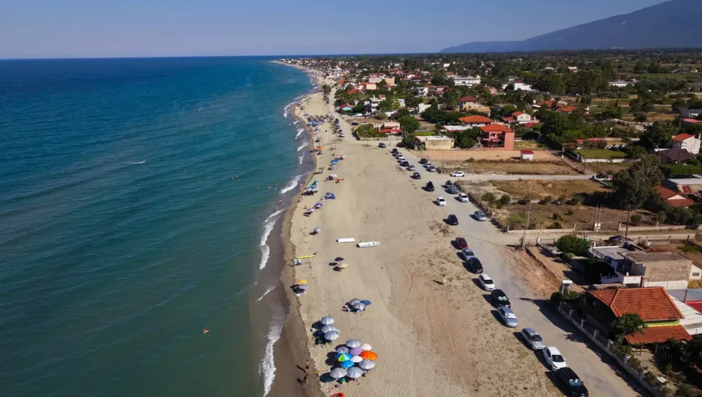 Εναέρια λήψη της παραλίας Καστρί Λουτρό στον Δήμο Τεμπών, με φαρδιά αμμουδιά, ρηχά νερά και ομπρέλες κατά μήκος της ακτής.