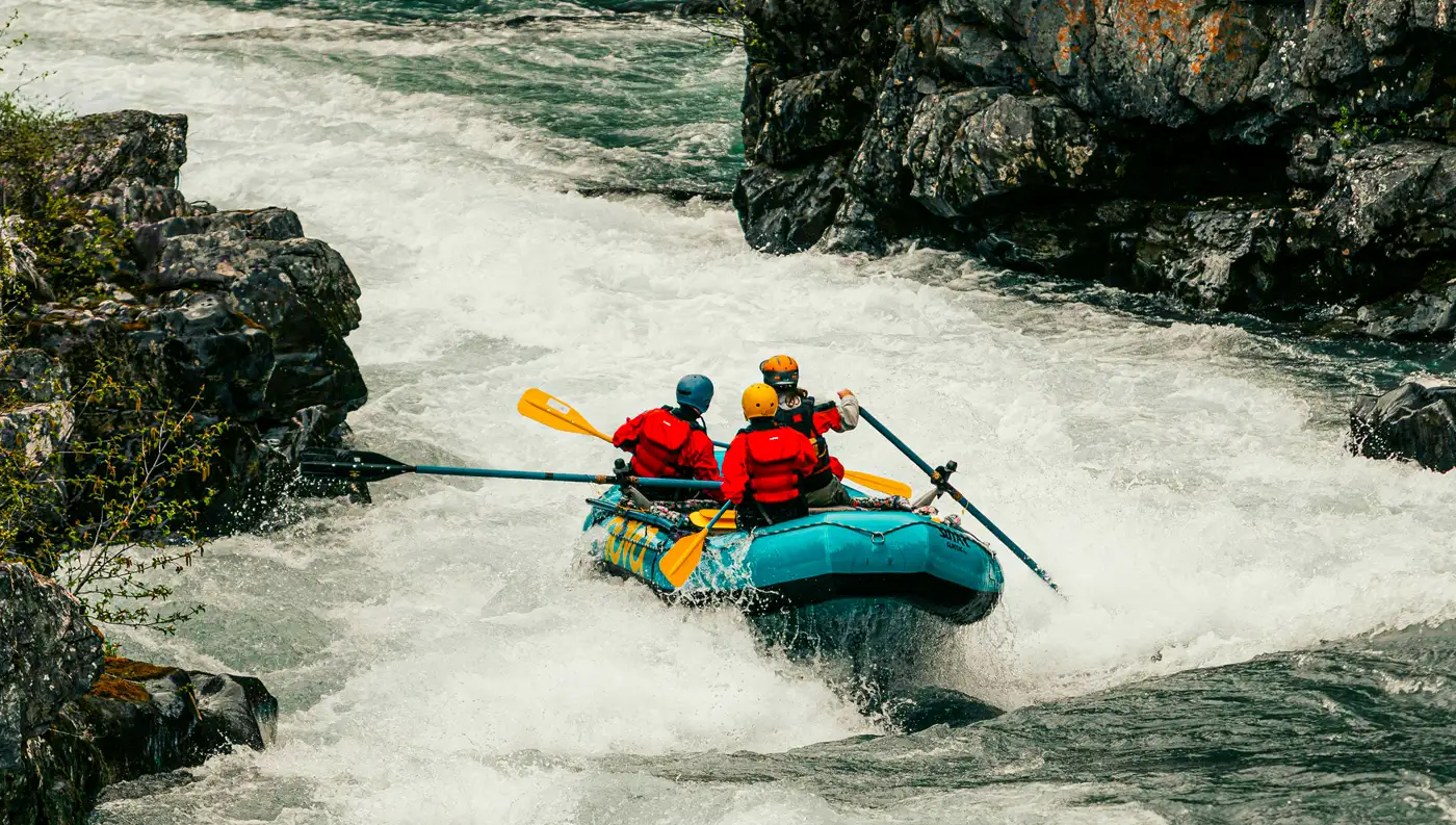 Φουσκωτή βάρκα rafting με τρεις κωπηλάτες να διασχίζει ορμητικά λευκά νερά σε στενό φαράγγι.
