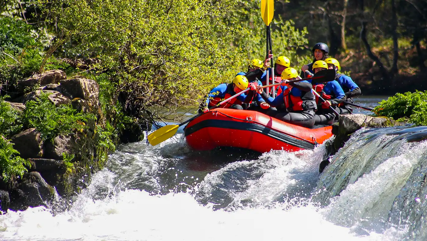 Ομάδα ατόμων σε κόκκινη βάρκα rafting κατά τη διάρκεια κατάβασης σε σημείο με έντονη ροή νερού.