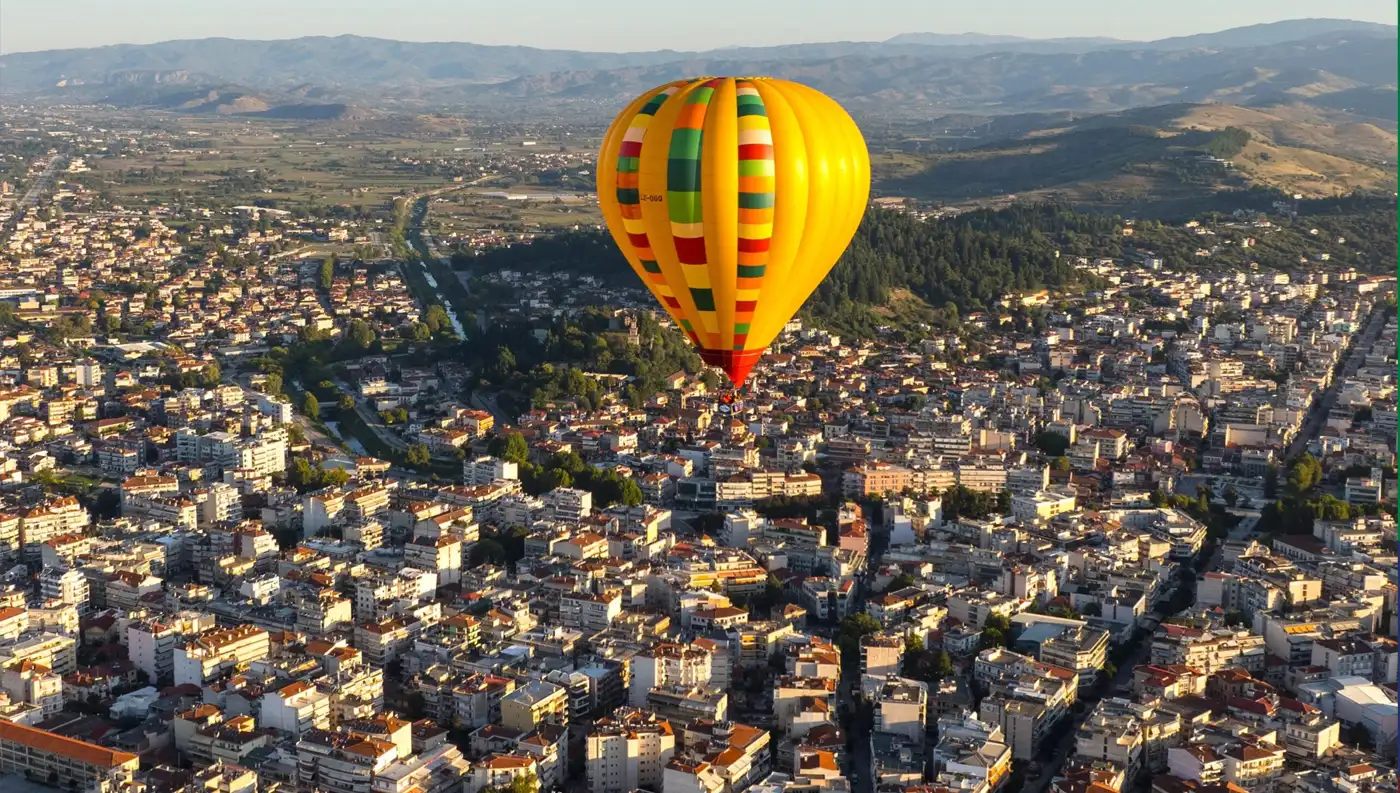 Κίτρινο αερόστατο πετάει ψηλά πάνω από την πόλη των Τρικάλων κατά το Thessaly Balloon Festival.