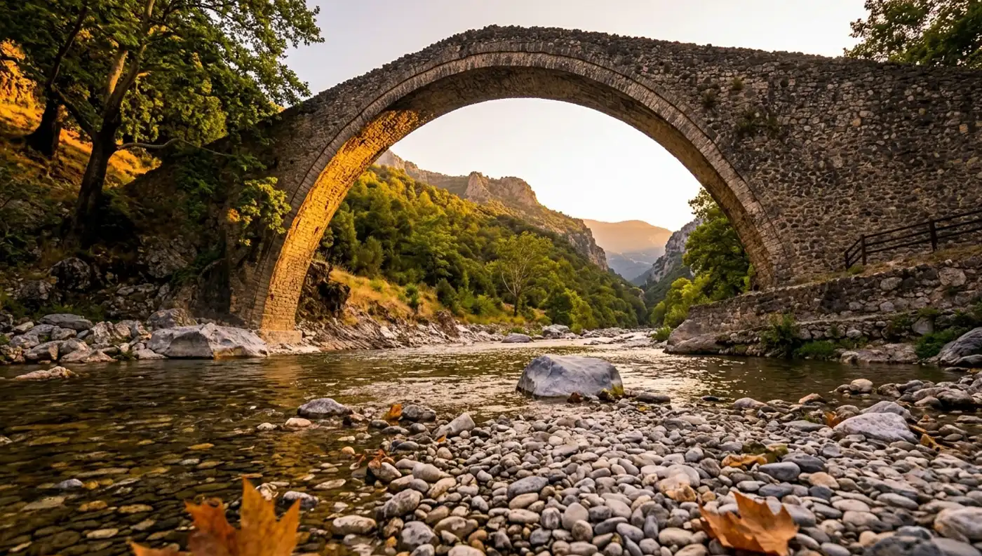 Το Γεφύρι της Πύλης φωτογραφημένο από χαμηλά μέσα από την κοίτη του ποταμού, με τα βότσαλα σε πρώτο πλάνο και τον ήλιο να φωτίζει το εσωτερικό του τόξου.