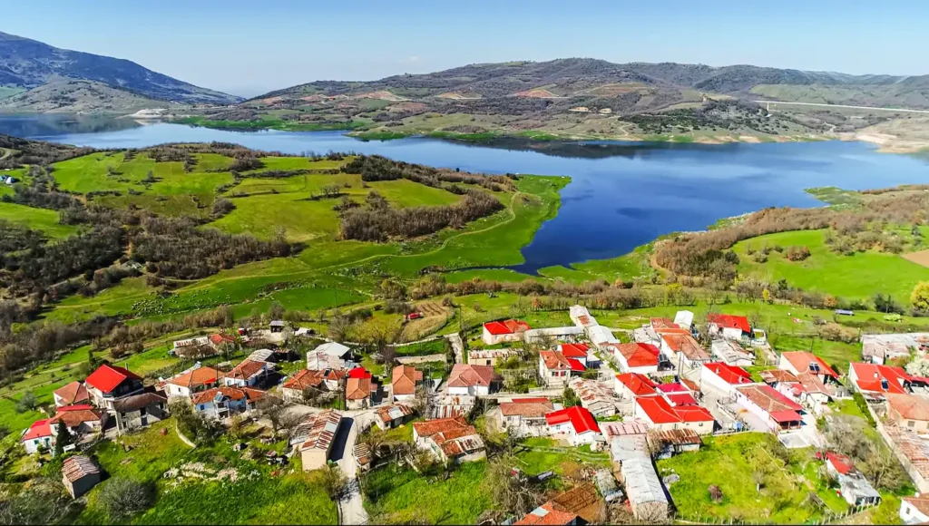 Πανοραμική εναέρια λήψη που δείχνει έναν παραδοσιακό οικισμό με κόκκινες στέγες και στο βάθος τα γαλάζια νερά στη Λίμνη Σμοκόβου.