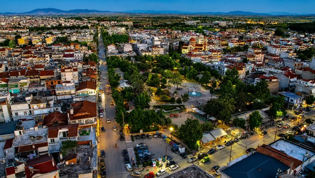 Εναέρια άποψη της κεντρικής δεντρόφυτης πλατείας της Νεάπολης και του αστικού ιστού κατά το σούρουπο.